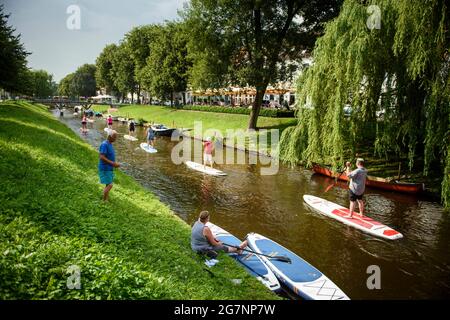 Friedrichstadt, Deutschland. Juli 2021. Mehrere Stand-up Paddler fahren bei sonnigem Wetter nacheinander durch einen Kanal. Quelle: Gregor Fischer/dpa/Alamy Live News Stockfoto