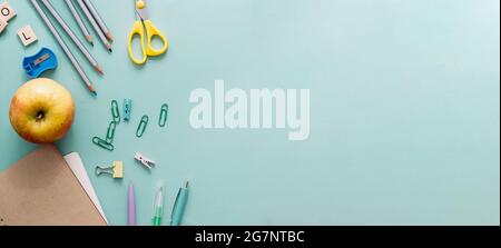 Zurück zum Schulkonzept. Buntstifte aus Holz, leeres Schulbuch, Büroklammern, Apfel und andere Schreibwaren auf blauem Hintergrund. Bleistifte zum Zeichnen Stockfoto