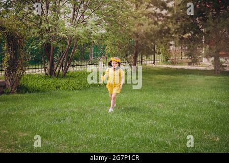 Ein Mädchen in einem gelben Kleid läuft auf dem grünen Gras und genießt einen Sommerurlaub mit ihrer Familie in ein warmes Land Stockfoto