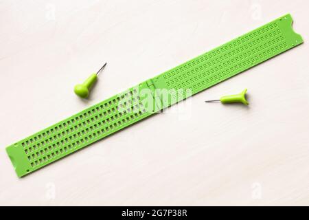 Draufsicht auf offenen leeren Plastikbraille-Schreibschiefer und Stift auf braunem Tisch Stockfoto