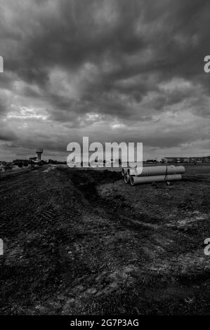 Gestapeltes Wasserhauptrohr mit Glockenanschluss neben einem freiliegenden Graben zur Installation Stockfoto