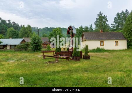 Alte, kleine Dorfhäuser und landwirtschaftliche Gebäude mitten im Wald. Schrein am Straßenrand im Vordergrund. Stockfoto