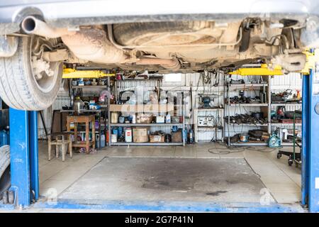 Ansicht von unten des angehobenen alten Fahrzeugs in der Autowerkstatt (Fokus auf den Schalldämpfer in der Mitte des Fahrzeugbodens) Stockfoto