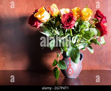 Frische rote und gelbe Rosen in Keramikkrug auf dunkelbraunem Holzhintergrund Stockfoto
