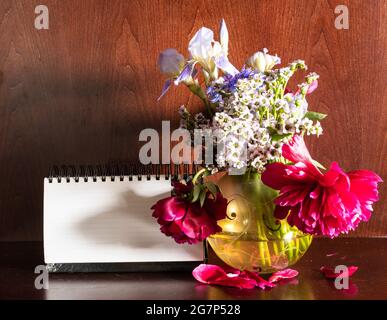 Frische Blumen in Vase und leerer Kalender auf dunkelbraunem Holzhintergrund Stockfoto