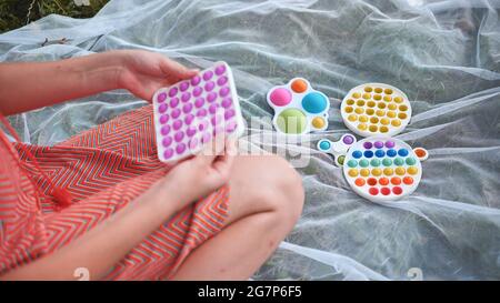 Teenager Mädchen spielt mit Anti-Stress-Spielzeug popit und einfache Grübchen im Park an einem Sommertag. Stockfoto