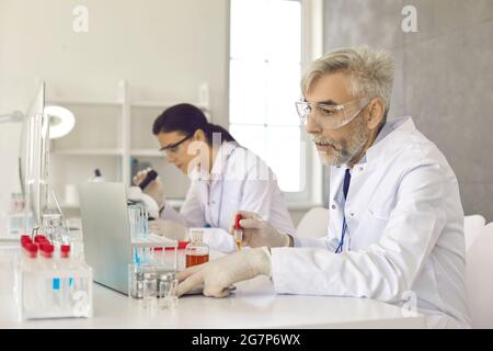 Ernsthafter Wissenschaftler, der Laptop verwendet, während er im medizinischen Labor an einem neuen Impfstoff arbeitet Stockfoto