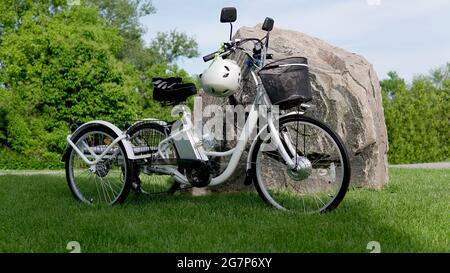 Elektrisches Trike oder E-Bike im Park an sonnigen Sommertagen. Von der Seite geschossen. Viel Licht. Die Ansicht des E-Motors und der Netzbatterie des Stockfoto