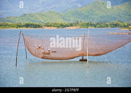 Großes Fischernetz im Wasser, mit lokalen Fischern in kleinen, von Menschen hergestellten Booten, Vietnam. Stockfoto