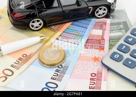 Ein Luxusauto mit Euro-Bargeld, mit einem Rechner und einem Stift als Symbol für die Fahrzeugfinanzierung. Stockfoto