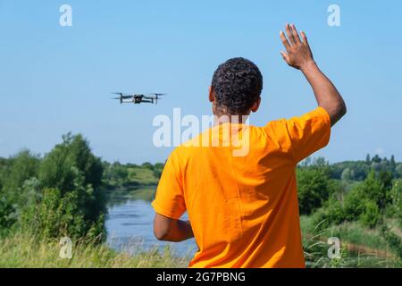 Afroamerikanischer Mann, der Drohne mit Controller auf der Wiese mit Rücken betreibt Stockfoto
