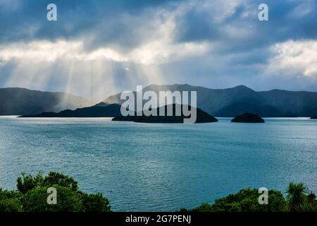 Über den Inseln in Waikawa Bay Picton brechen bei nebligen Regenfällen Sonnenstrahlen durch die Wolken Stockfoto