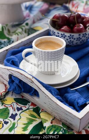 Nahaufnahme eines Kaffees in einer eleganten Keramikschale mit einer verschwommenen Schüssel voller Kirschen daneben. Stockfoto