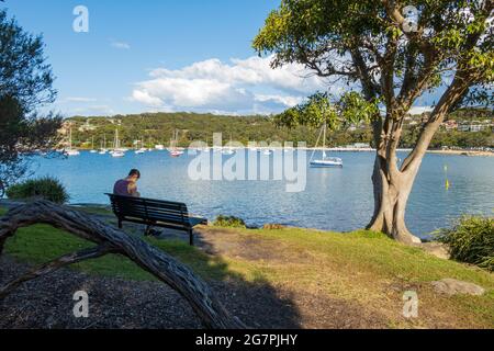 Mann sitzt und entspannt an einem sonnigen Tag am Balmoral Beach, Sydney, Australien, während der Pandemie-Sperre Stockfoto