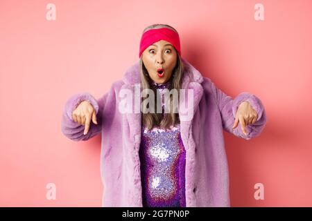 Mode- und Shopping-Konzept. Beeindruckt asiatische weibliche Zeigefinger nach unten und Blick aufgeregt bei der Kamera, zeigt genial promo Angebot, stehen über Stockfoto