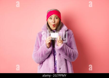 Shopping- und Modekonzept. Bild von erstaunt asiatische ältere Frau Auschecken Promo-Angebot, halten Kunststoff-Kreditkarte und starren beeindruckt in die Kamera Stockfoto