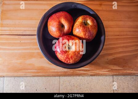 Nahaufnahme mehrerer reifer, reicher, frischer, organischer, saftiger roter Äpfel in einer schwarzen Keramikschale auf einem Holztisch. Kopierbereich.Selektiver Fokus. Stockfoto