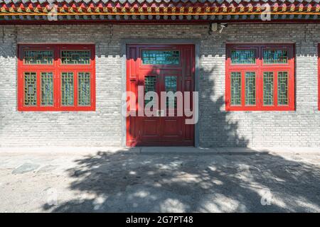 Backsteinmauer und rote Holztür und Fensterhintergrund eines alten Gebäudes Stockfoto