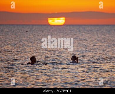 Portobello, Edinburgh, Schottland, Großbritannien. Juli 2021. Sonnenaufgangsschönheit am Meer. Temperatur 14 Grad. Dieses Paar genießt ein Bad im Morgengrauen im Firth of Forth. Quelle: Arch White/Alamy Live News. Stockfoto