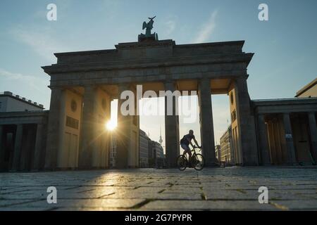 Berlin, Deutschland. Juli 2021. Ein Radfahrer fährt bei Sonnenaufgang durch das Brandenburger Tor. Quelle: Jörg Carstensen/dpa/Alamy Live News Stockfoto