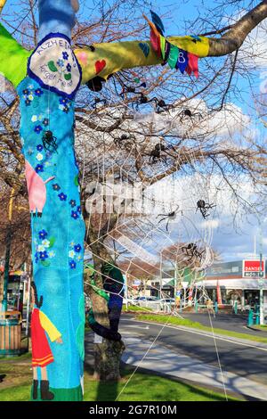 „Yarn Bombing“ oder gestrickte Street Art auf einem Baum. Dieses Beispiel zeigt die Alzheimers Society Forget-me-Not und ein Spinnennetz Stockfoto