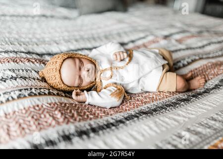 Wiedergeborene Babypuppe, die auf einem Bett mit gemustertem Dovetbezug und einer Haube liegt, Model Release ist nicht erforderlich, da Baby eine lebensechte Puppe ist Stockfoto