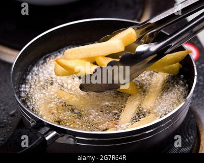 Nahaufnahme der Pommes Frites in der Fritteuse in heißem Öl auf dem Elektroherd in der Küche. Hausgemachte pommes frites zubereiten. Stockfoto