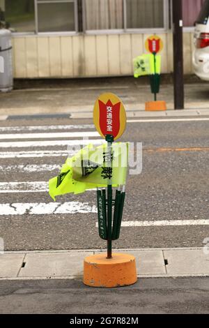 Gelbe Fußgängerflaggen, mit einem Straßenübergang, der am Inawashiro-See einsatzbereit ist. 'Crossing' ist auf Japanisch geschrieben. Stockfoto