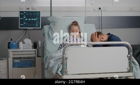 Stationäre kranke Tochter schläft nach einer medizinischen Operation, während Vater besorgt für die Gesundheit Erholung beten. Kind mit Nasenschlauch, der während der Untersuchung auf der Krankenstation im Bett liegt Stockfoto