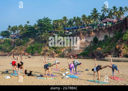 Gruppe westlicher Reisender, die am Strand unter der Klippe, Varkala, Kerala, Indien, Yoga praktizieren Stockfoto