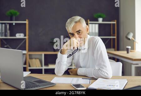 Porträt eines erfolgreichen, zufriedenen Geschäftsmannes, der an seinem Arbeitsplatz im Büro sitzt. Stockfoto