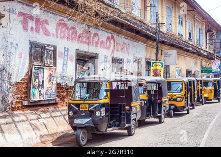 Eine Reihe von Auto-Rikschas Reihen sich in der Straße vor dem Lagerhaus mit bollywood-Filmplakat an der Wand, Fort Kochi (cochin), Kerala, Indien Stockfoto