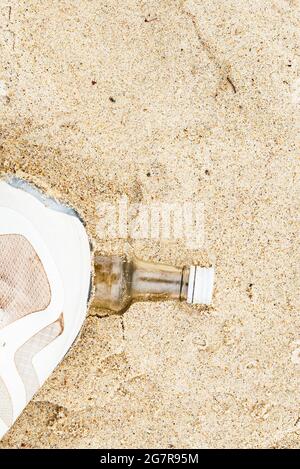 Eine echte Glasflasche am Strand, die mit einem Sneakerbein in den Sand gepresst wurde Stockfoto