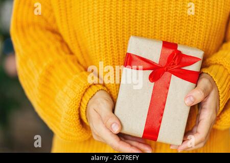 Frau in kuscheligen gelben Strickpullover geben weihnachten Handwerk Geschenkboxen mit rotem Band. Geben Geschenke Konzept.Valentinstag und Muttertag Geschenk-Konzept Stockfoto