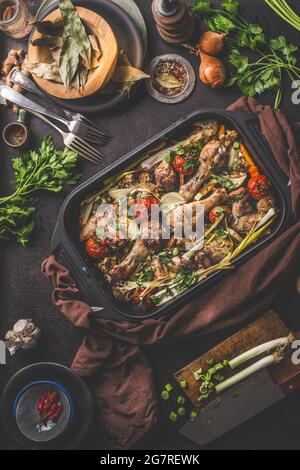 Leckere gebratene Hähnchendrumsticks mit Gemüse in gusseiserner Auflaufform auf Küchentisch-Hintergrund mit aromatischen Kräutern, Gewürzen und Zutaten. Top Vie Stockfoto
