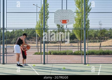 Basketballtrainer zeigt einem Kind mit einer Beinprothese, wie man Basketball schießt. Coach, der ein Kind trainiert. Stockfoto