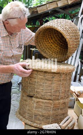 13. Juli 2021, Sachsen-Anhalt, Holzdorf-Jessen: In seinem rund 5000 Quadratmeter großen Freiwaldgarten steht Förster und Waldpädagoge Detlef Schulze an einem über 100 Jahre alten Bienenstock. Der historische Korb ist Teil seiner Gartendekoration, die in der großen Fläche bewundert werden kann. Detlef Schulze hat sich für 40 um seine Wohlfühloase gesorgt, die mit rund 100 Bäumen und Sträuchern sowie vielen gestalteten und geschnitzten Details jederzeit für Besucher zugänglich ist. Foto: Waltraud Grubitzsch/dpa-Zentralbild/ZB Stockfoto