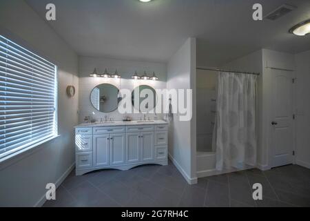 Großes Master-Badezimmer mit weißen Wänden und schräg gefliesten Böden in Grau Stockfoto