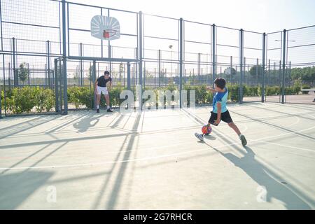 Zwei Brüder spielen Fußball. Der ältere Bruder ist der Torwart und der jüngere tritt eine Strafe und hat eine Beinprothese. Stockfoto