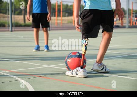 Nicht erkennbare Kinder, die Fußball spielen, eines von ihnen hat eine Beinprothese. Geschwister spielen zusammen Sport. Stockfoto