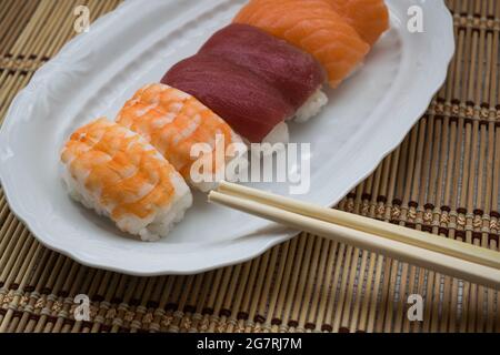 Mehrere Sushi-Stücke auf einem weißen Teller mit Essstäbchen Stockfoto