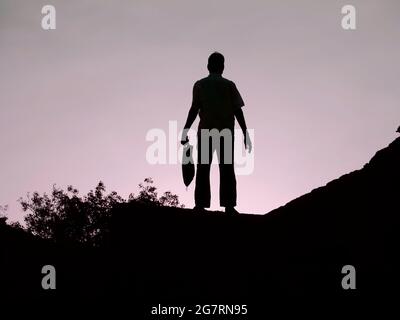 Ein alter indischer Mann hält Tasche auf der linken Hand auf Silhouette Himmel Natur Hintergrund, Lifestyle-Konzept Bild Stockfoto