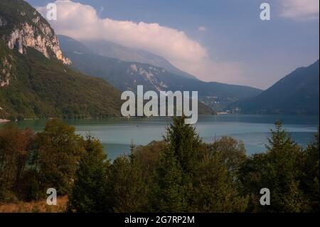 Herbstfärbungen tauchen im September in den dichten Wäldern und der Vegetation am Wasser auf, die den ‘schönsten See Italiens’, den Lago di Molveno in Trentino-Südtirol, umgeben. Der See, umgeben von den Gipfeln und Klippen der Brenta-Dolomiten, wurde 1890 vom italienischen Dichter und Schriftsteller Antonio Fogazzaro als „die kostbare Perle in einer noch kostbareren Schatulle“ beschrieben. Das bis zu 124 m (406 ft) tiefe, ruhige Wasser verbirgt einen versteinerten Wald, der vor etwa 3,000 Jahren, während der frühen Eisenzeit, eingetaucht war. Stockfoto