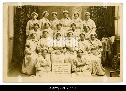 Postkarte aus der Zeit des 1. Weltkriegs mit Munitionsarbeitern, die in einem gefährlichen Job arbeiten, da das Schild auf der Vorderseite des Gruppenfotos zeigt, dass „Munition Workers Gaines Filling Factory Dangerous Buildings Woolwich Arsenal“ diese Munitionetten tragen Abzeichen „on war Service“. Postkarte datiert / veröffentlicht 1917, Woolwich, London, Großbritannien im Zusammenhang mit Artilleriemunition aus dem Ersten Weltkrieg waren 'gaines' instabile Sprengstoffe, die oft als Grundierung oder Zünder in Granaten verwendet wurden, meist in Verbindung mit anderen Sprengstoffen. Der Arsenal Football Club wurde 1886 als Munition Workers' Team aus Woolwich gegründet. Stockfoto