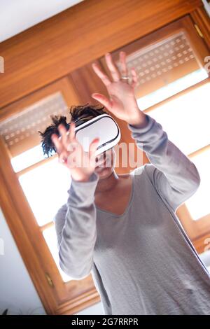 Porträt einer aktiven jungen schwarzen Frau, die einen Virtual-Reality-Simulator in einem Raum zu Hause testet. Technologie- und Lifestyle-Konzepte. Stockfoto
