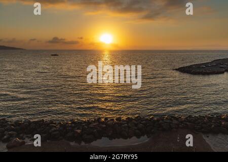 Schöner Sonnenuntergang über dem Meer und Strand voller Sonnenschirme mit Sonne hinter Wolken Stockfoto