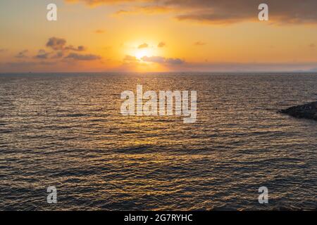 Schöner Sonnenuntergang über dem Meer mit Sonne hinter Wolken Stockfoto