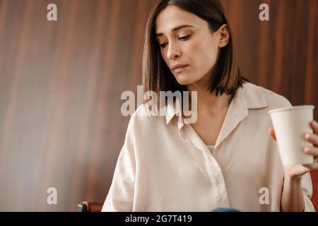 Junge Frau trinkt Kaffee, während sie im Sessel sitzt Stockfoto