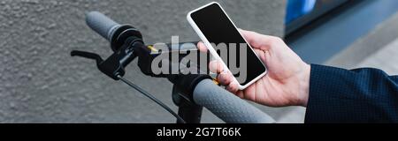 Beschnittene Ansicht eines reifen Geschäftsmannes mit Smartphone und leerem Bildschirm in der Nähe des E-Scooters, Banner Stockfoto