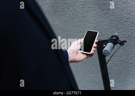 Teilansicht eines reifen Mannes mit Smartphone und leerem Bildschirm in der Nähe des E-Scooters Stockfoto